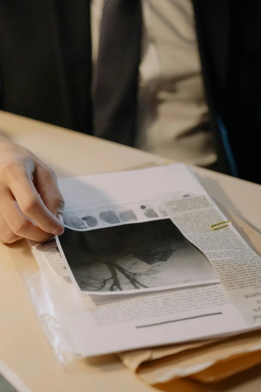 a man sitting at a table reading a newspaper, a photocopy, inspired by René Burri, unsplash, hyperrealism, diary on her hand, medical dissection, holographic material, 70mm film screenshot