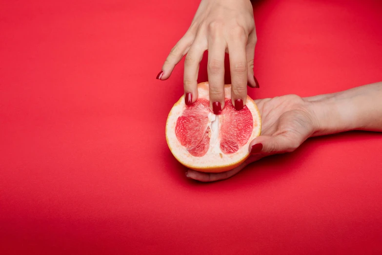 a close up of a person holding a grapefruit, an album cover, by Julia Pishtar, homoeroticism, red theme, only two hands, wolfy nail