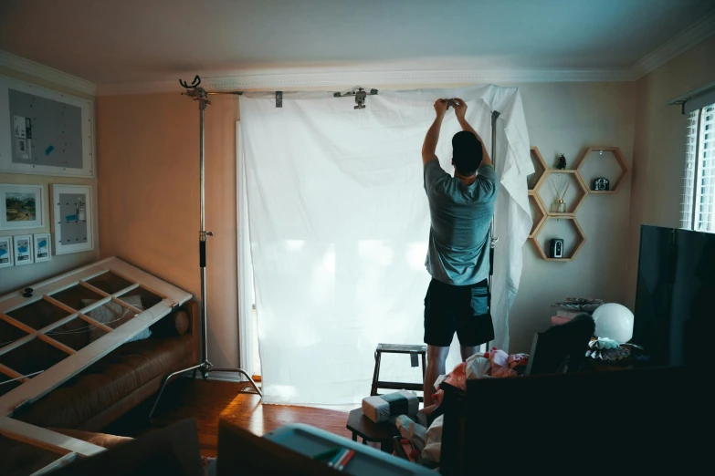 a man standing on a ladder in a living room, pexels contest winner, fully covered in drapes, screen light, making of, timelapse