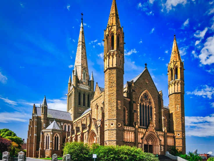a large church with two steeples in front of a blue sky, inspired by Alfred East, pexels contest winner, north melbourne street, tall stone spires, reddish, exterior