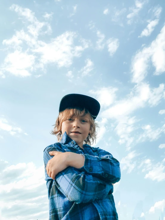 a little boy that is standing in the grass, an album cover, trending on pexels, symbolism, wearing a flannel shirt, with overhead cloudy!!!!! skies, small hat, androgynous person