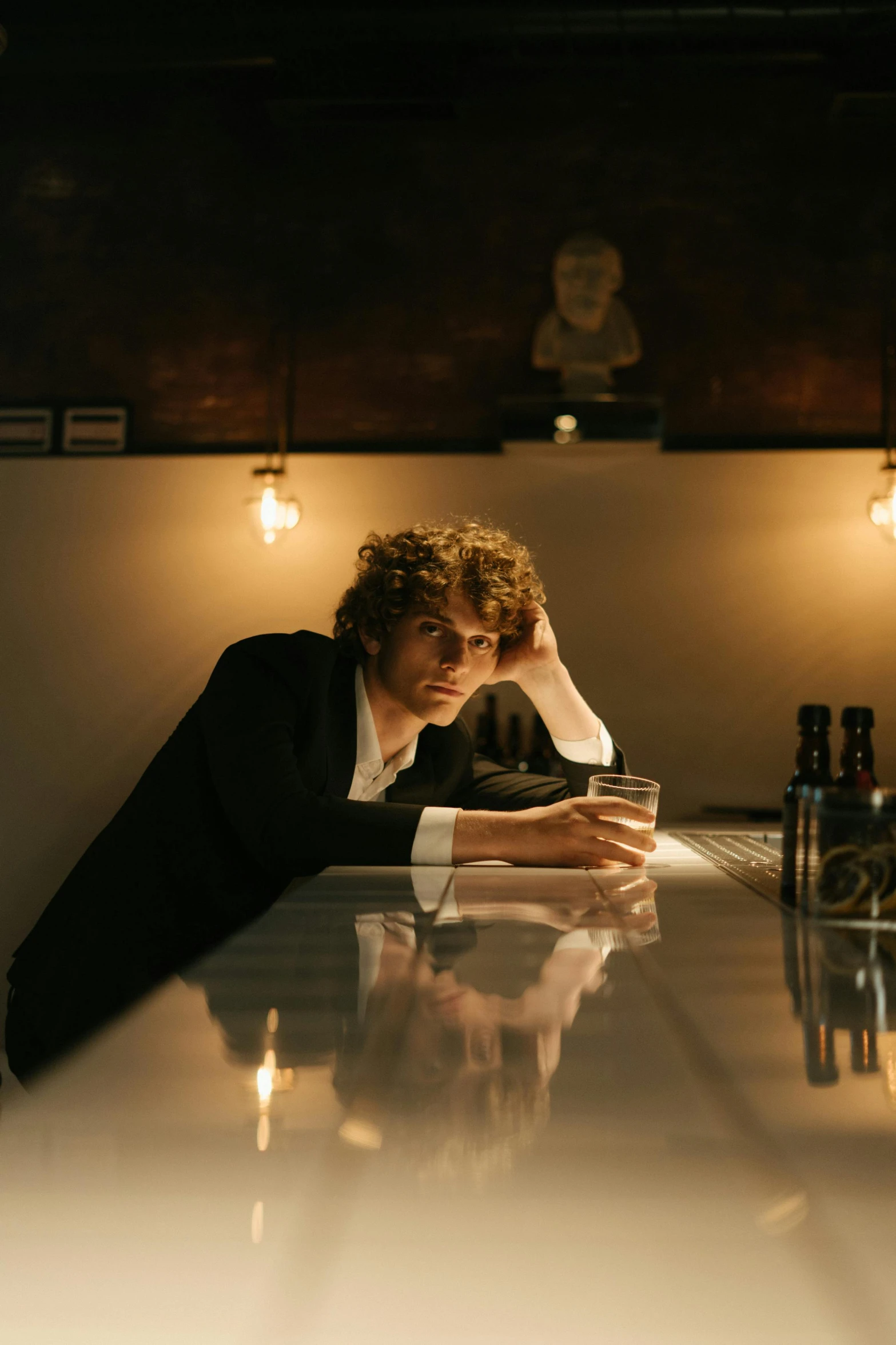 a man sitting at a bar with a glass of wine, an album cover, unsplash, renaissance, pale skin curly blond hair, serious business, ignant, low key lights