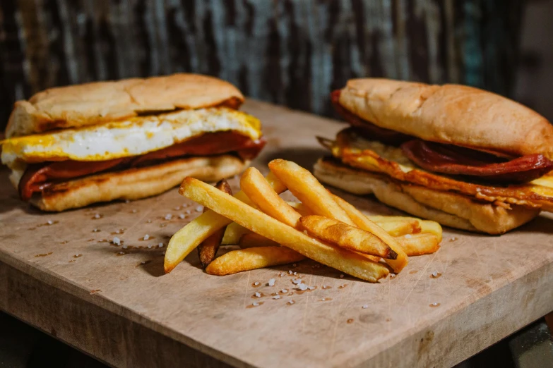 a couple of sandwiches and french fries on a cutting board, a portrait, by Lee Loughridge, pexels, breakfast buffet, 🦩🪐🐞👩🏻🦳, woodfired, chilean