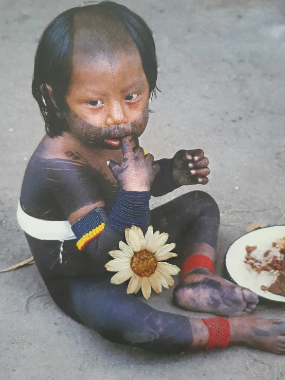 a young child sitting on the ground next to a plate of food, an album cover, inspired by Steve McCurry, sumatraism, holding a flower, tribal facepaint, 1 9 8 5 photograph, made of tar