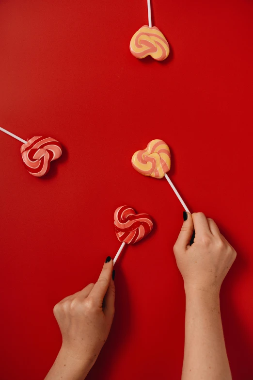 two hands holding lollipops on a red surface, inspired by Ödön Márffy, trending on pexels, intricate pasta waves, hearts, 🐿🍸🍋
