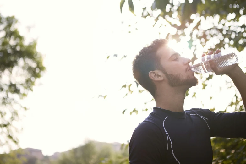 a man drinking water out of a plastic bottle, by Julian Allen, shutterstock, sun flare, against the backdrop of trees, profile image, athletic muscle tone