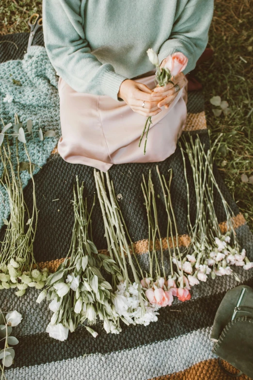 a woman sitting on a blanket holding a bunch of flowers, inspired by Elsa Bleda, trending on unsplash, renaissance, green and pink fabric, crafting, woman made of plants, stems