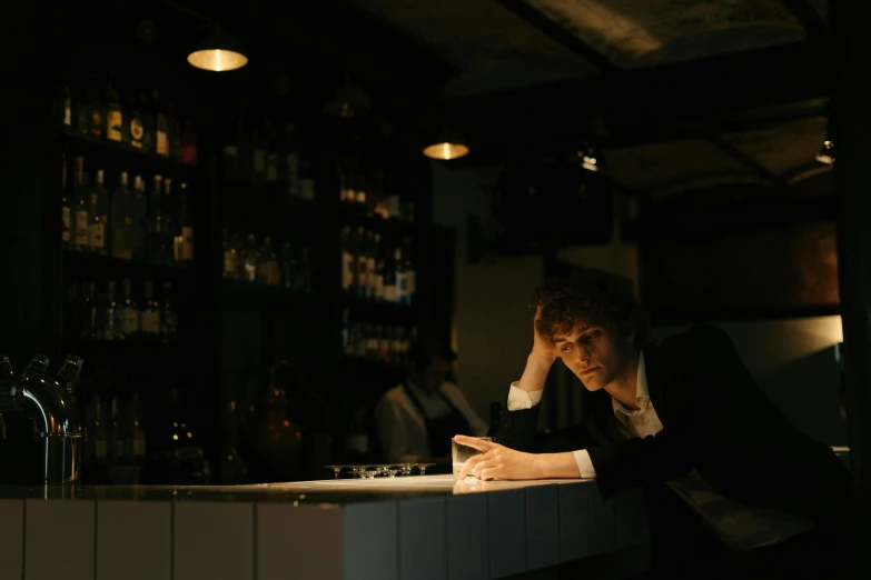 a man sitting at a bar writing on a piece of paper, a portrait, unsplash, cinema still, standing in a dimly lit room, lachlan bailey, max dennison