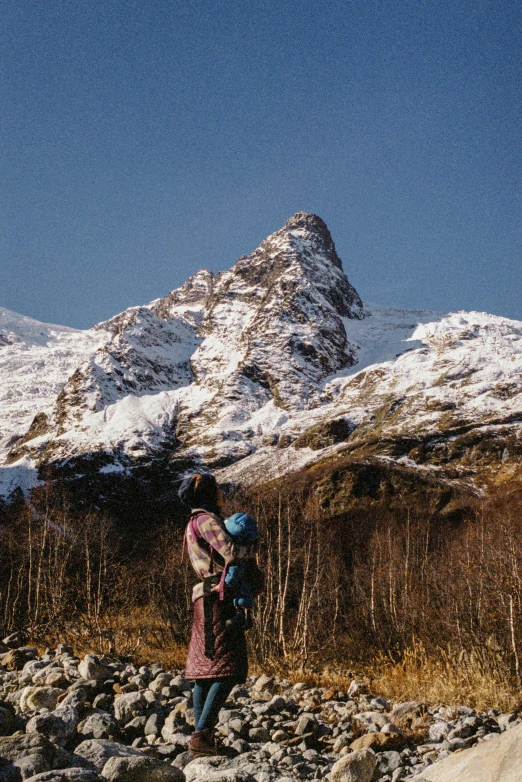 a person standing in a rocky area with mountains in the background, taken on a 1990s camera, stålenhag, towering above a small person, seen from a distance