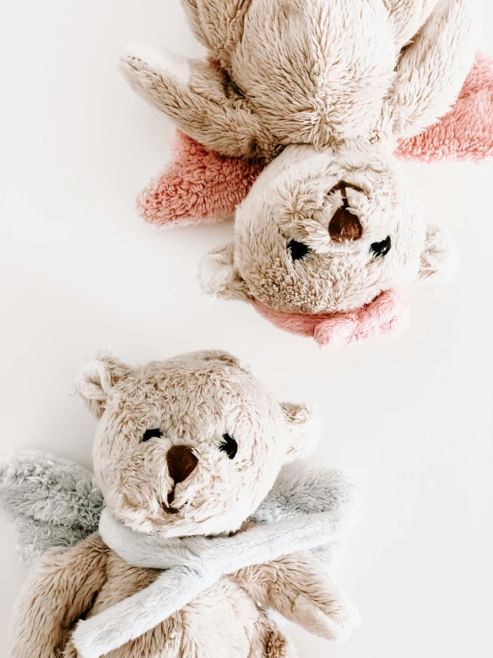 a couple of teddy bears sitting next to each other, trending on pexels, silver angel wings, top down angle, bedhead, soft colours