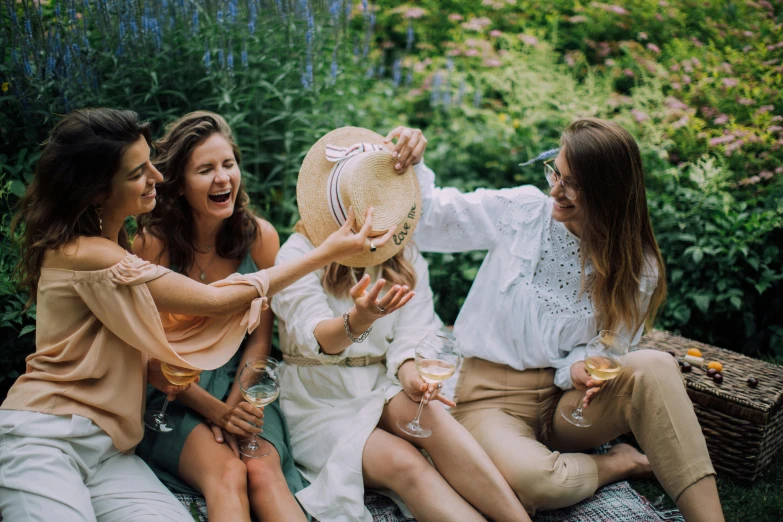 a group of women sitting on top of a grass covered field, by Emma Andijewska, pexels contest winner, happening, holding glass of wine, sitting in the rose garden, wearing a linen shirt, flirting