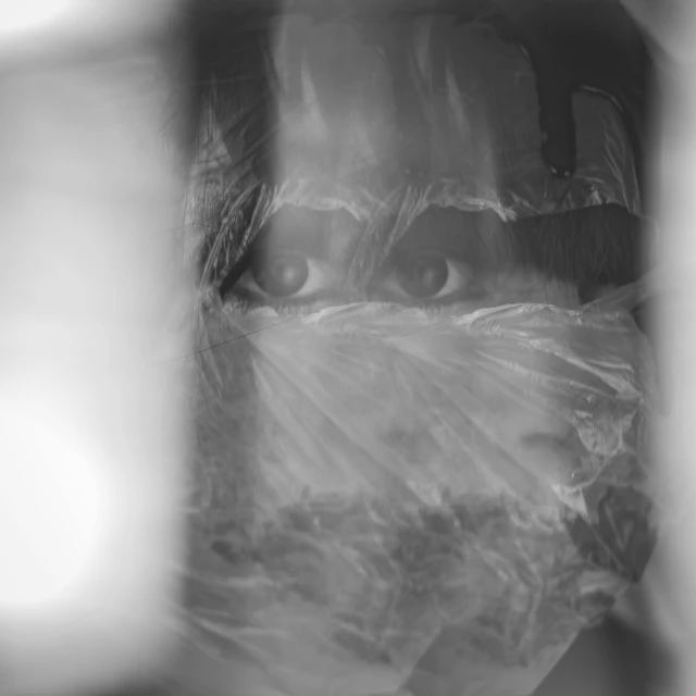 a black and white photo of a woman wrapped in plastic, a picture, by Emma Andijewska, plasticien, face covers half of the frame, looking at you, blur effect face, scientist