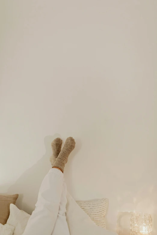 a person laying on a bed with their feet up, by Elsa Bleda, pexels contest winner, beige colors, scandinavian, neutral background, standing on a shelf