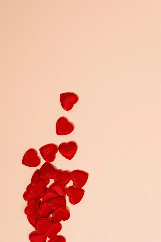 a vase filled with red rose petals on top of a table, by Carey Morris, pexels, romanticism, hearts symbol, in front of an orange background, pink hearts in the background, a high angle shot