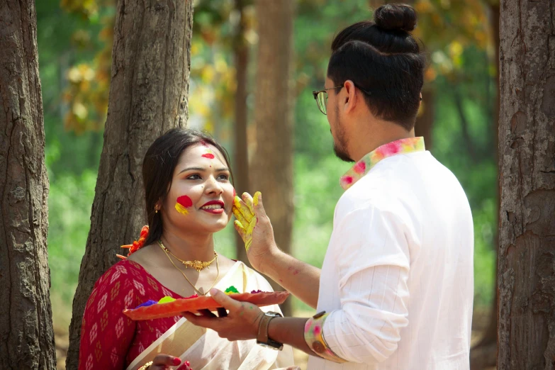 a man standing next to a woman in a forest, pexels contest winner, hurufiyya, wearing bihu dress mekhela sador, face painting, eating, tie-dye