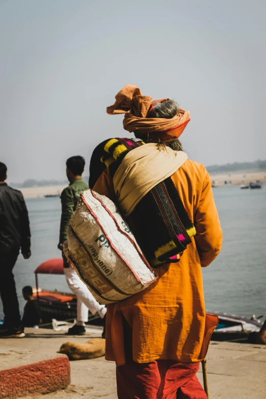 a group of people standing next to a body of water, bags, turban, over the shoulder view, travel guide