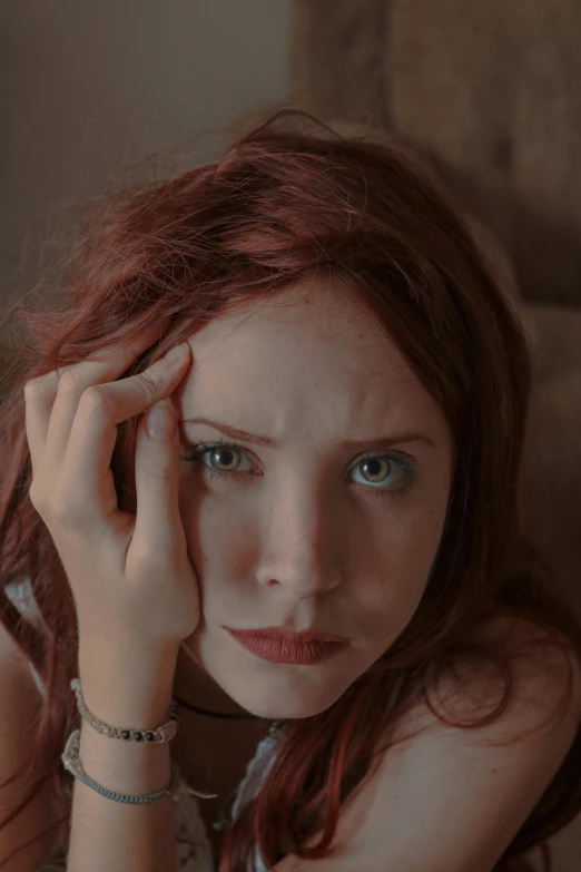 a woman sitting on a couch with her hand on her head, trending on reddit, renaissance, crimson red hair and red eyes, film still promotional image, portrait of depressed teen, red contact lenses