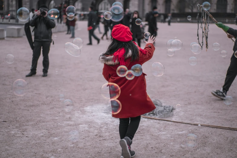 a little girl in a red coat blowing bubbles, pexels contest winner, visual art, people walking around, circles, casual game, foamy bubbles