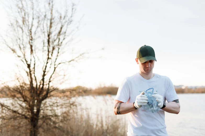 a man standing next to a body of water, a portrait, unsplash, process art, working out in the field, scattered rubbish, avatar image, pekka halonen