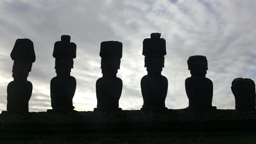 a group of statues sitting on top of a grass covered field, a statue, moai, silhouetted, multiple stories, no cropping