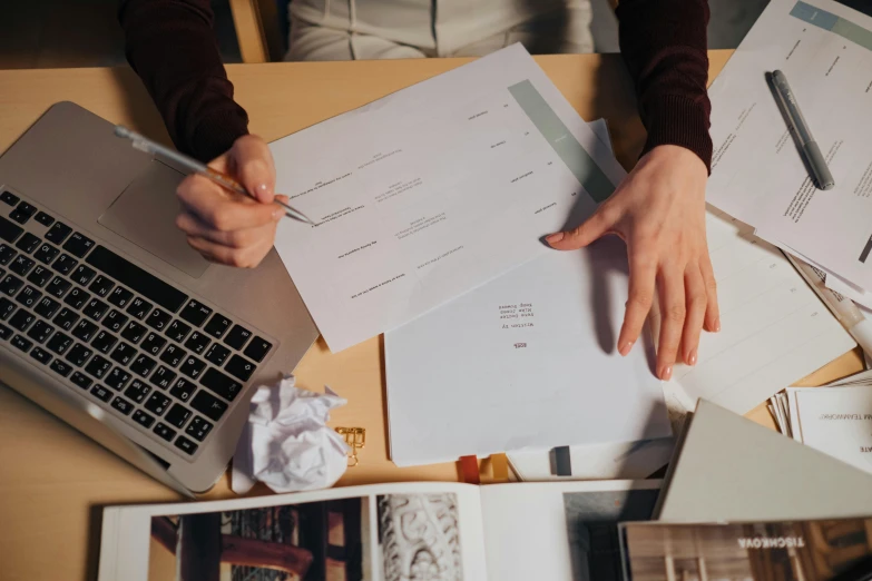 a person sitting at a table with a laptop and papers, by Julia Pishtar, epic design, filling the frame, 9 9 designs, sheet of paper