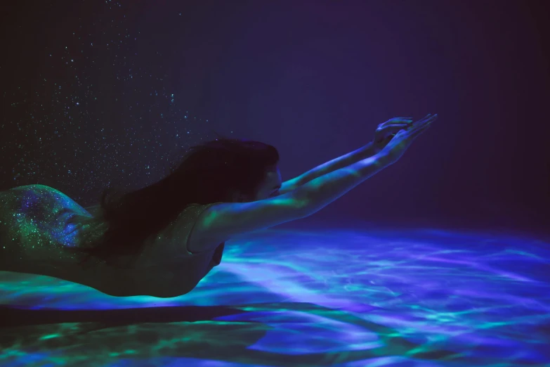 a woman that is laying down in the water, by Elsa Bleda, pexels contest winner, holography, blue and purple lighting, weightlessness, closeup cinematic aquatic scene, 5 feet away