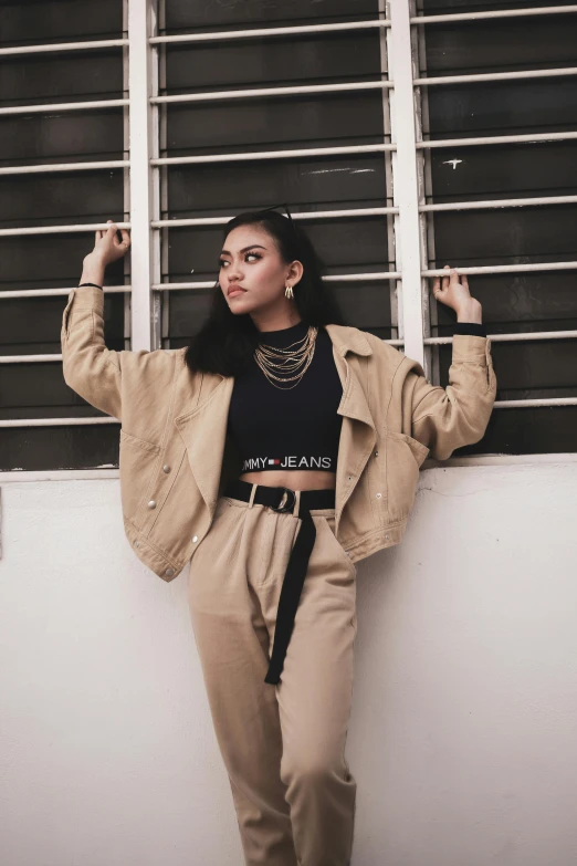 a woman leaning against a wall in front of a window, an album cover, by Robbie Trevino, trending on pexels, cropped shirt with jacket, casual streetwear, tan suit, joy ang