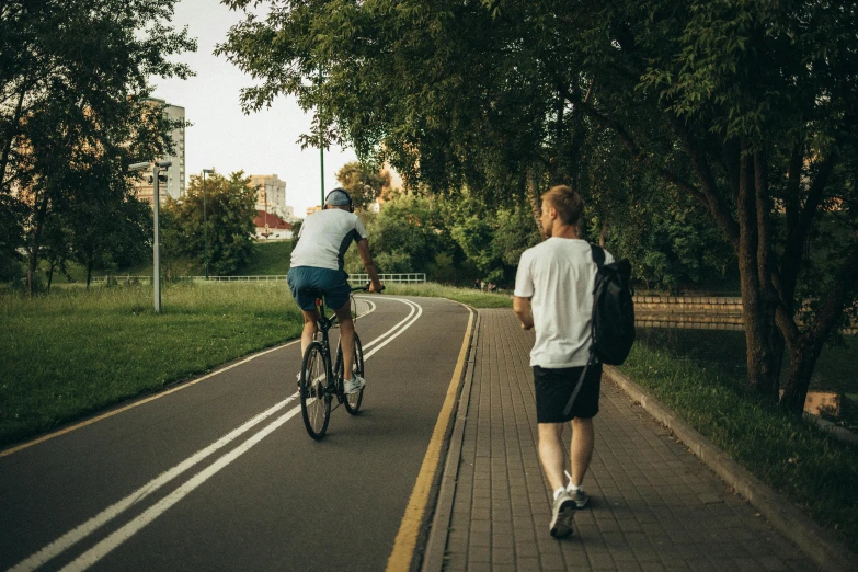 a couple of people riding bikes down a street, by Adam Marczyński, pexels contest winner, with a park in the background, with his back turned, sports clothing, man walking