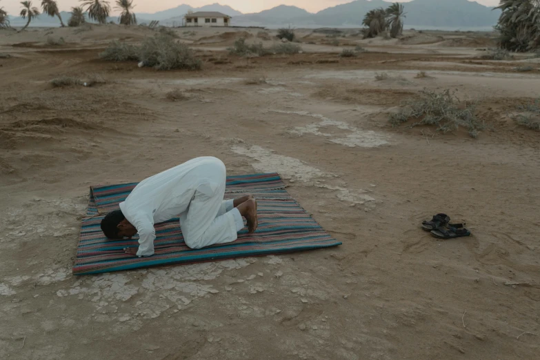 a man is laying on a blanket in the desert, pexels contest winner, hurufiyya, praying posture, still from film, aida muluneh, bent over posture