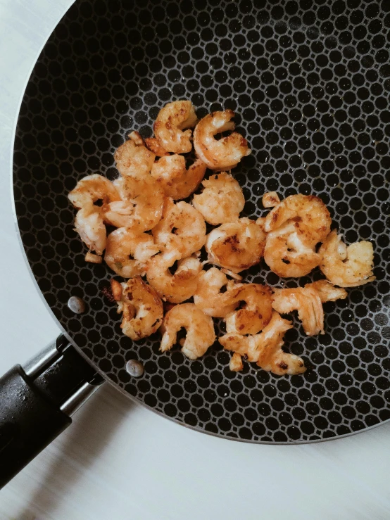 a frying pan filled with shrimp sitting on top of a counter, by Carey Morris, trending on unsplash, small freckles, deconstructed waffle, petals, precise stippling