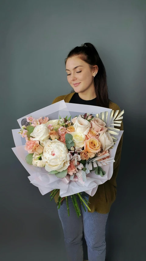 a woman holding a large bouquet of flowers, on a gray background, monika, in shades of peach, cream paper