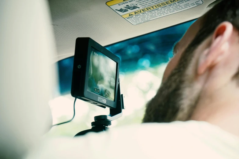 a man that is sitting in the back seat of a car, close up to the screen, with back to the camera, square, digital photograph