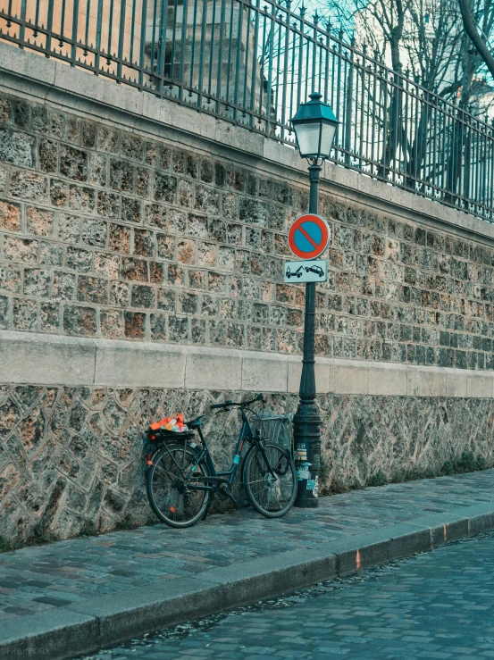 a bike leaning against a stone wall next to a lamp post, a photo, pexels contest winner, paris city, traffic signs, low quality photo, full frame image