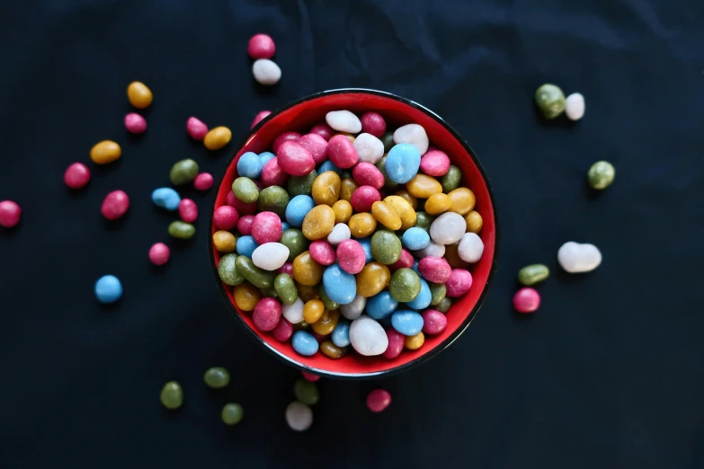 a red bowl filled with lots of colorful candies, by Joe Bowler, pexels contest winner, alien capsules, pearls, on a dark background, pink and blue colour