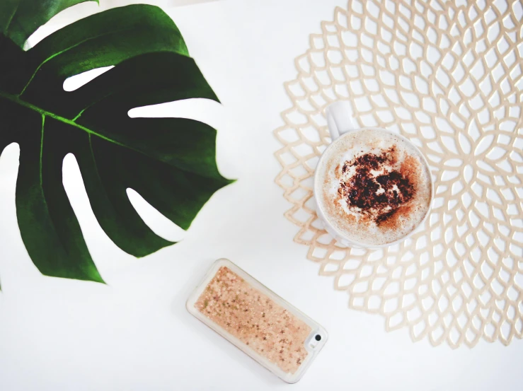 a cup of coffee sitting on top of a white table, trending on unsplash, tropical leaves, cell phone photo, full of sand and glitter, pixel art”