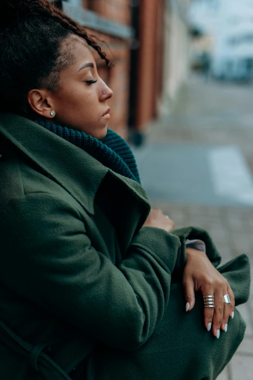 a woman sitting on the side of a street, trending on pexels, renaissance, wearing green jacket, comforting, african american woman, wearing hunter coat