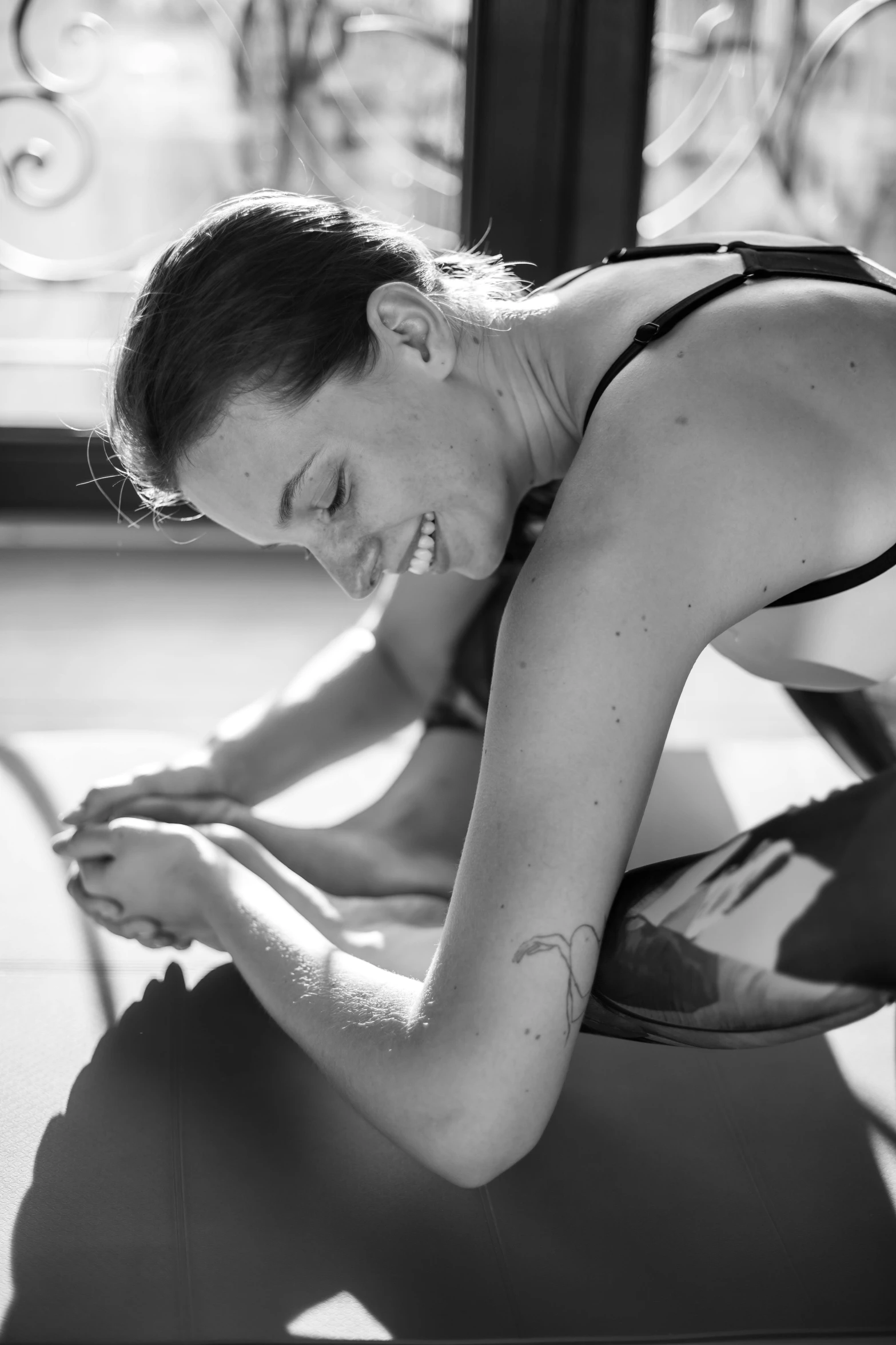 a black and white photo of a woman on a yoga mat, cheeky smile, hands pressed together in bow, sun shining, ink