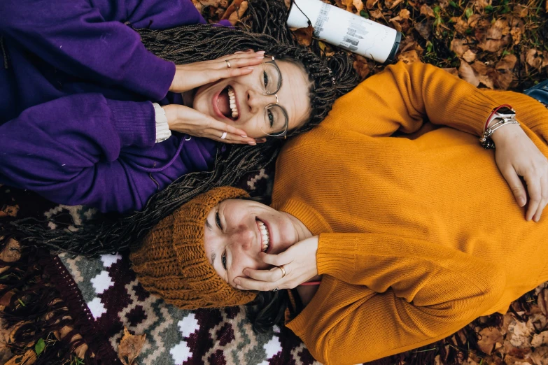 a man and a woman laying on a blanket in the leaves, by Julia Pishtar, trending on pexels, antipodeans, wearing a beanie, happy friend, skincare, background image