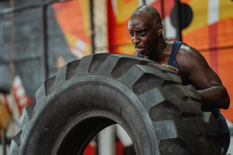 a man holding a large tire in a gym, a portrait, pexels contest winner, mkbhd as iron man, sweaty and dirty, foreground background, origin jumpworks