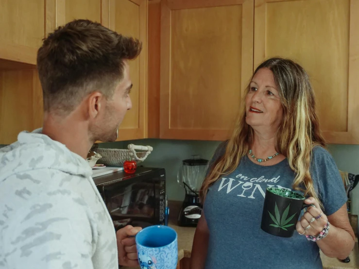 a man and a woman standing in a kitchen, wearing a marijuana t - shirt, next to a cup, casey cooke, profile image