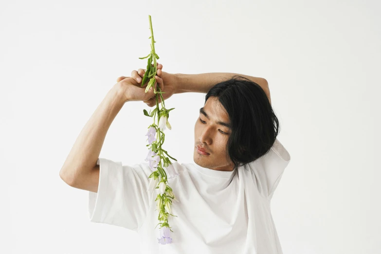 a man holding a flower in front of his head, an album cover, inspired by Kanō Naizen, trending on pexels, dressed in a white t-shirt, product introduction photo, natural fragile pose, botanical herbarium