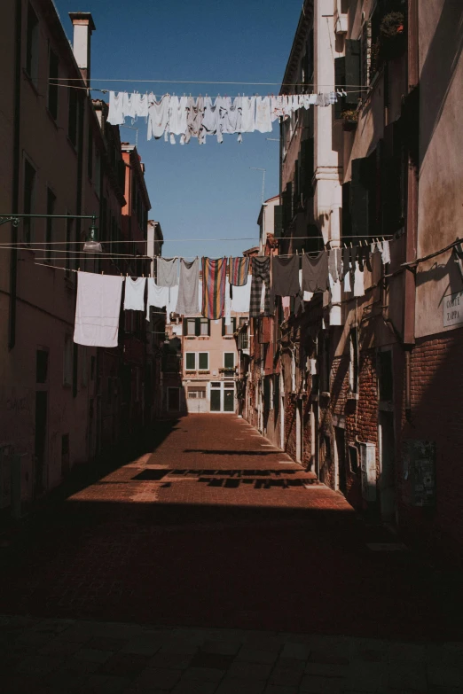 a narrow street with clothes hanging out to dry, unsplash contest winner, renaissance, burnt sienna and venetian red, late afternoon light, album cover, dirty clothes