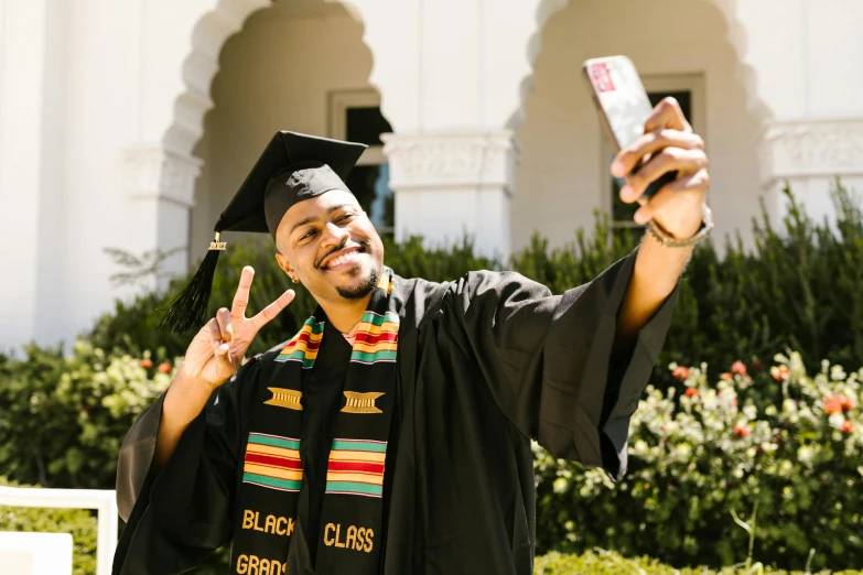 a man in a graduation cap and gown taking a selfie, brown skinned, embroidered robes, bay area, 2022 photograph