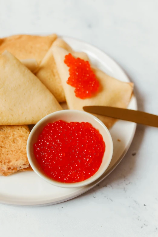 a white plate topped with pancakes and red cavia, by Julia Pishtar, reddit, renaissance, red caviar instead of sand, close-up product photo, brood spreading, russian and japanese mix