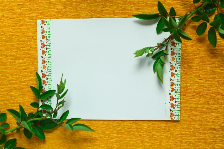 a piece of paper sitting on top of a wooden table, by Julia Pishtar, trending on pixabay, mail art, orange plants, border pattern, ribbon, green