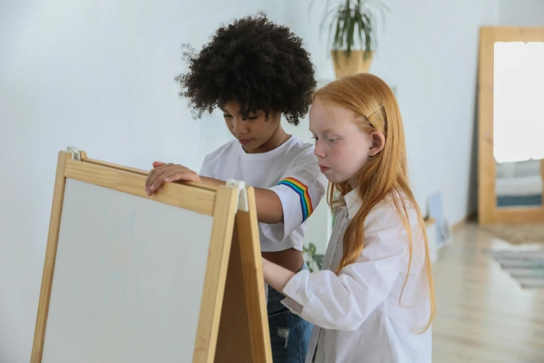 a couple of kids that are standing in front of a easel, pexels contest winner, interactive art, white wall coloured workshop, young girls, whiteboard, on a white table