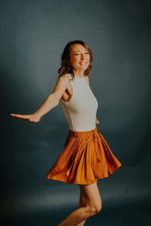 a woman in an orange skirt posing for a picture, pexels contest winner, arabesque, plain background, lighthearted, pleated miniskirt, brown