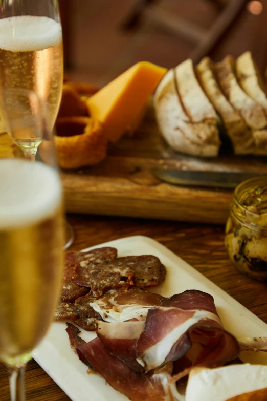 a wooden table topped with plates of food and glasses of wine, beer glasses, thumbnail, bull, cheeses