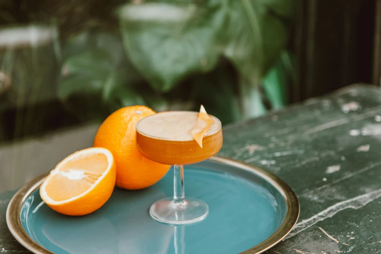 a couple of oranges sitting on top of a blue plate, cocktail in an engraved glass, waist up, press shot, sunday afternoon