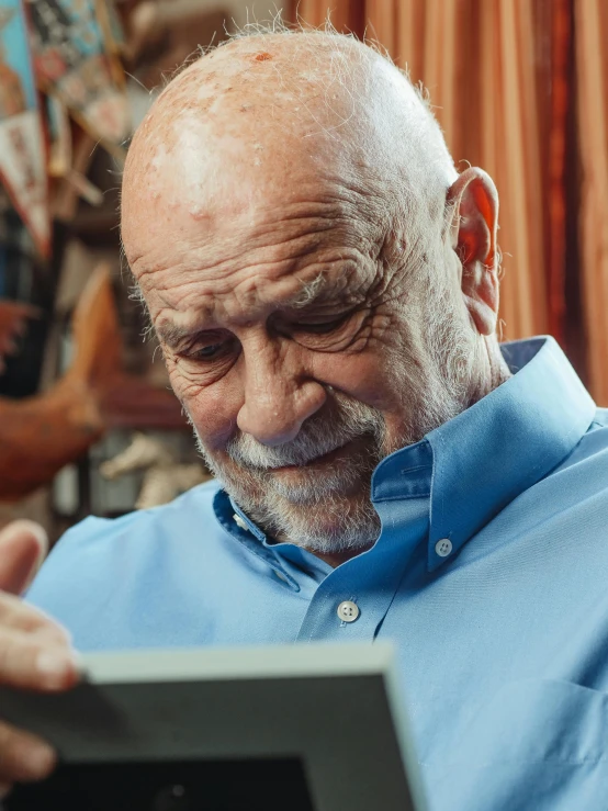 a man in a blue shirt is looking at a tablet, a portrait, by Everett Warner, pexels contest winner, mike ehrmantraut, a still of a happy, profile image, very old